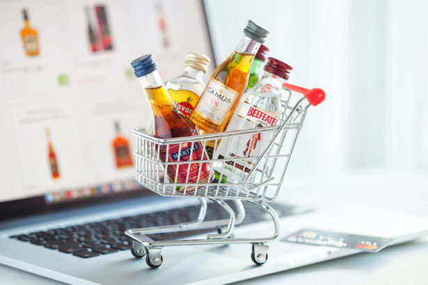 Minsk, Belarus - January 16, 2018: Illustrative editorial photo of shopping cart full of small alcohol bottles -  Camus and Martell cognacs, Havana club rum, Beefeater gin on laptop. Minsk, Belarus.